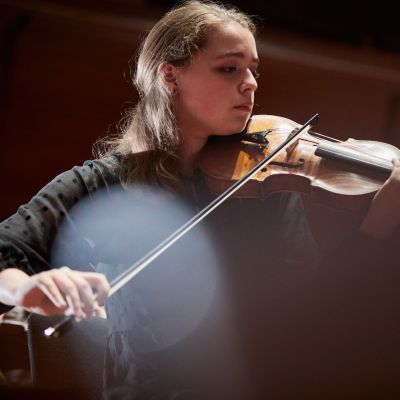A girl with brown hair and wearing a black long sleeved top plays the violin.